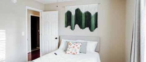A bedroom with a bed, a ceiling fan, a wall-mounted artwork, and a door leading to another room.