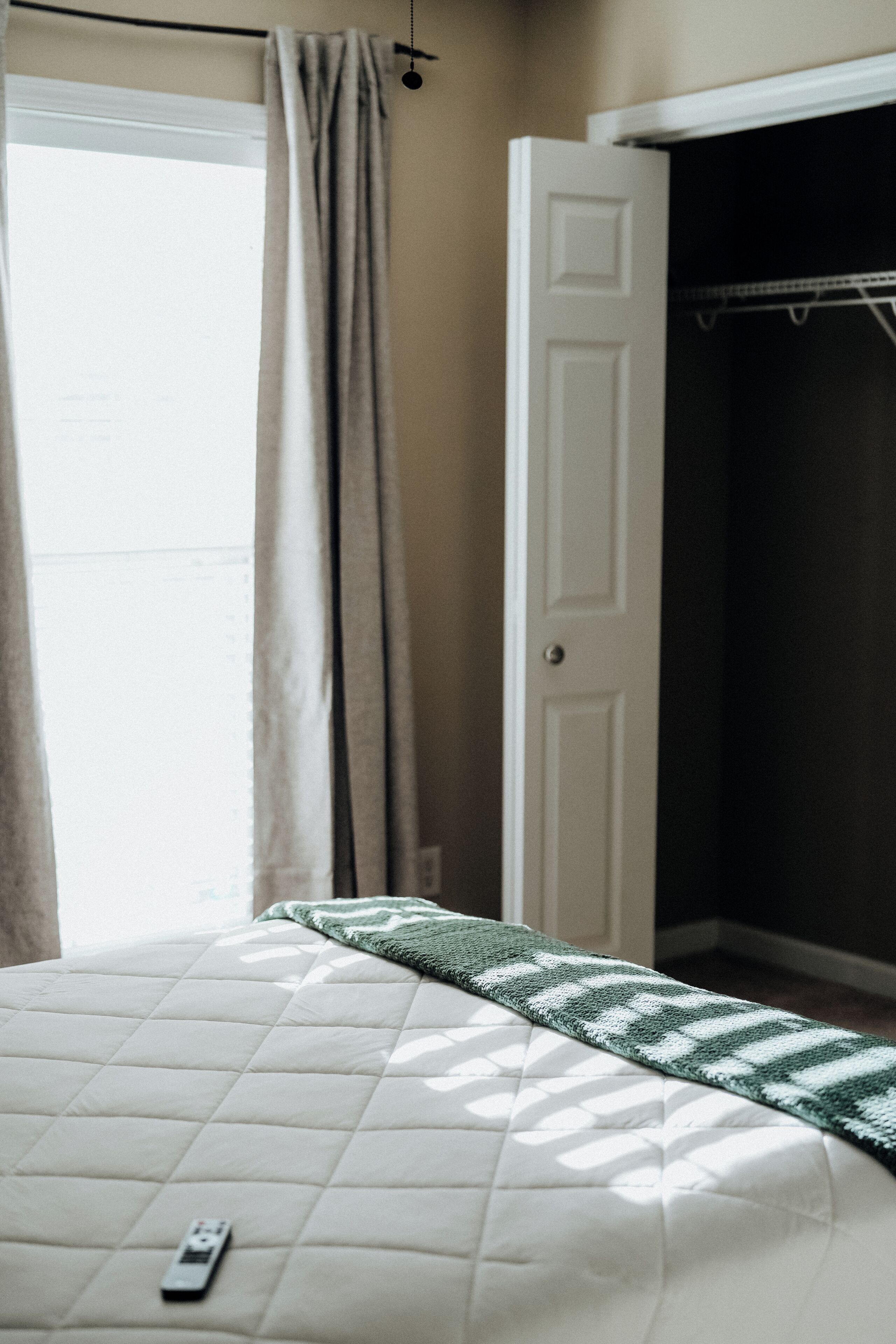 Une chambre à coucher avec un lit, une télécommande, une armoire et une fenêtre avec des rideaux.