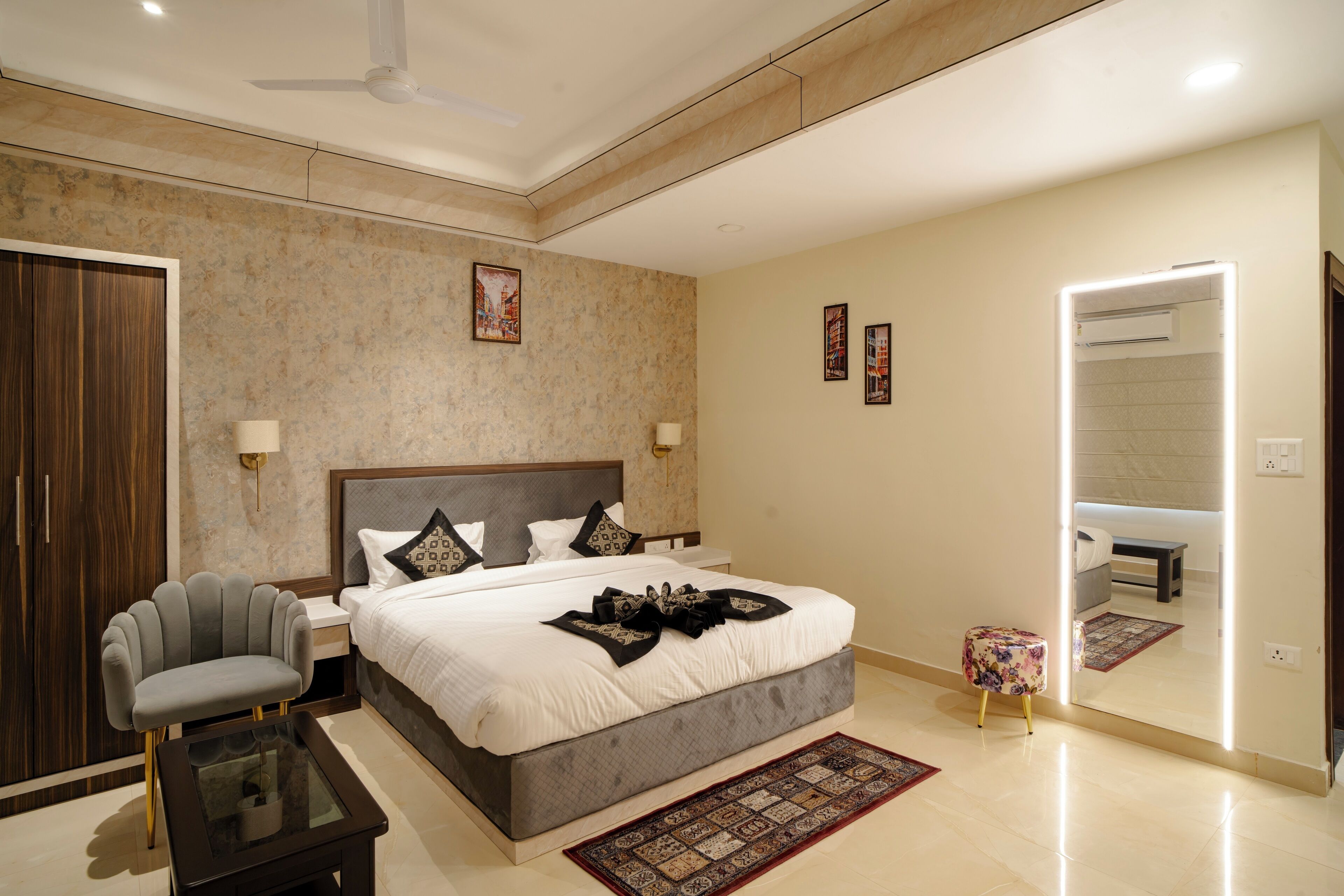 A modern bedroom with a large bed, bedside lamps, a small table, a chair, and a mirror.