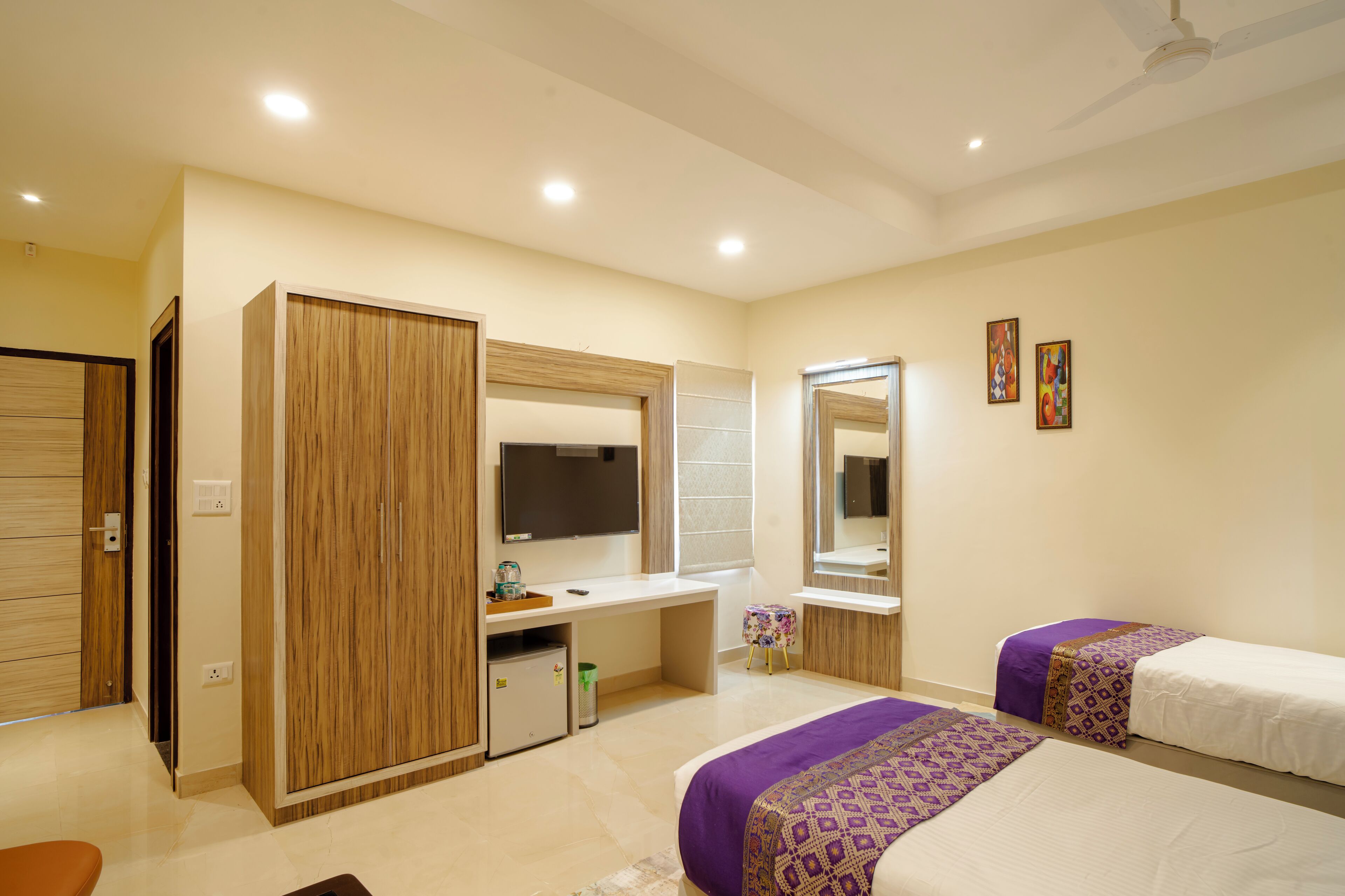 A modern bedroom with a desk, two beds, a wardrobe, and a mirror.