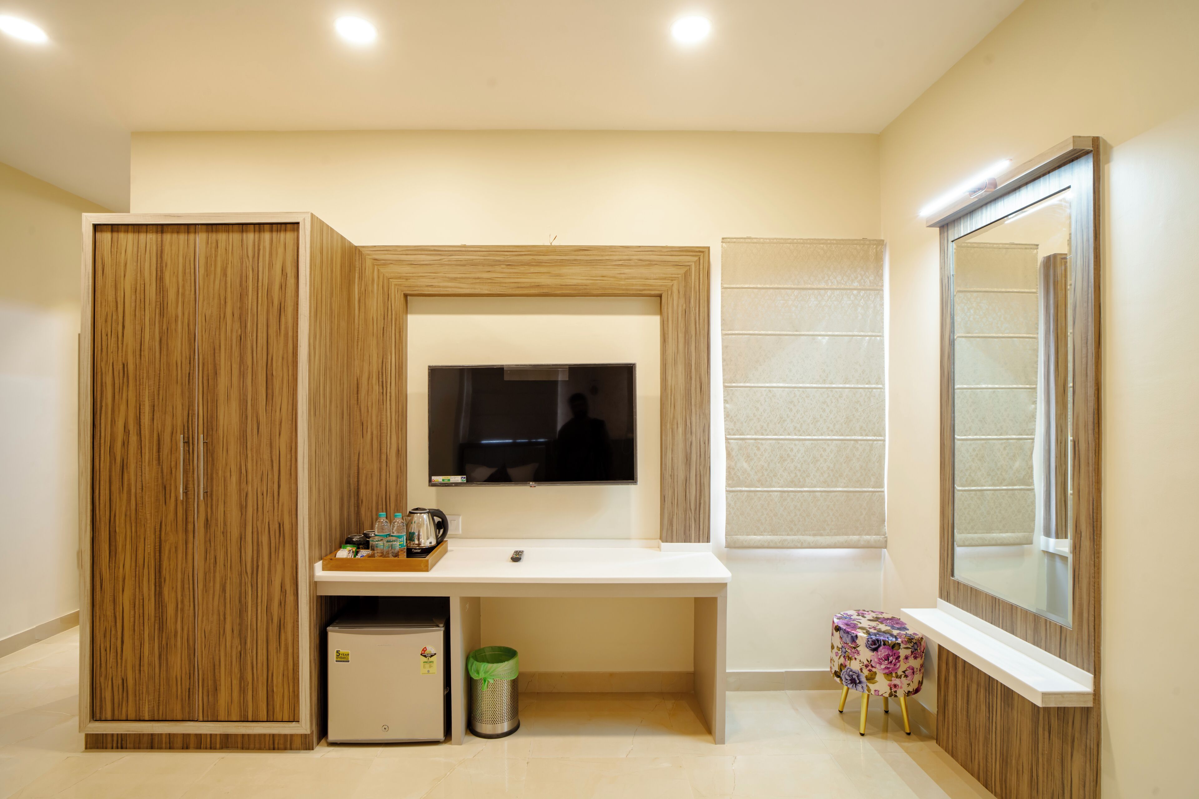A modern bathroom with a wooden vanity, a mirror, a television, and a small trash bin.