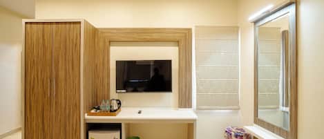 A modern bathroom with a wooden vanity, a mirror, a television, and a small trash bin.