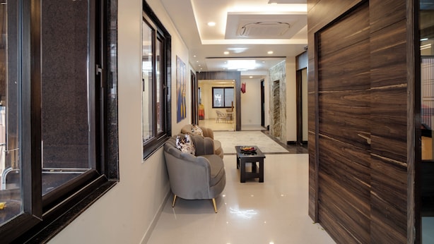 A modern hallway with a grey armchair, a small table, and a wooden door. - Omkar International Hotel (VARANASI)