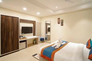 A hotel room with a bed, a wardrobe, a desk with a mirror, and a television.