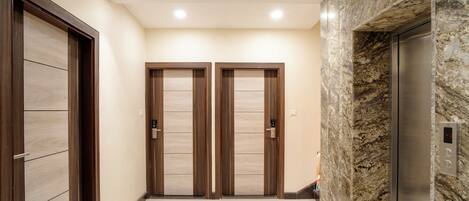 A hallway with two wooden doors and a marble wall with an elevator.