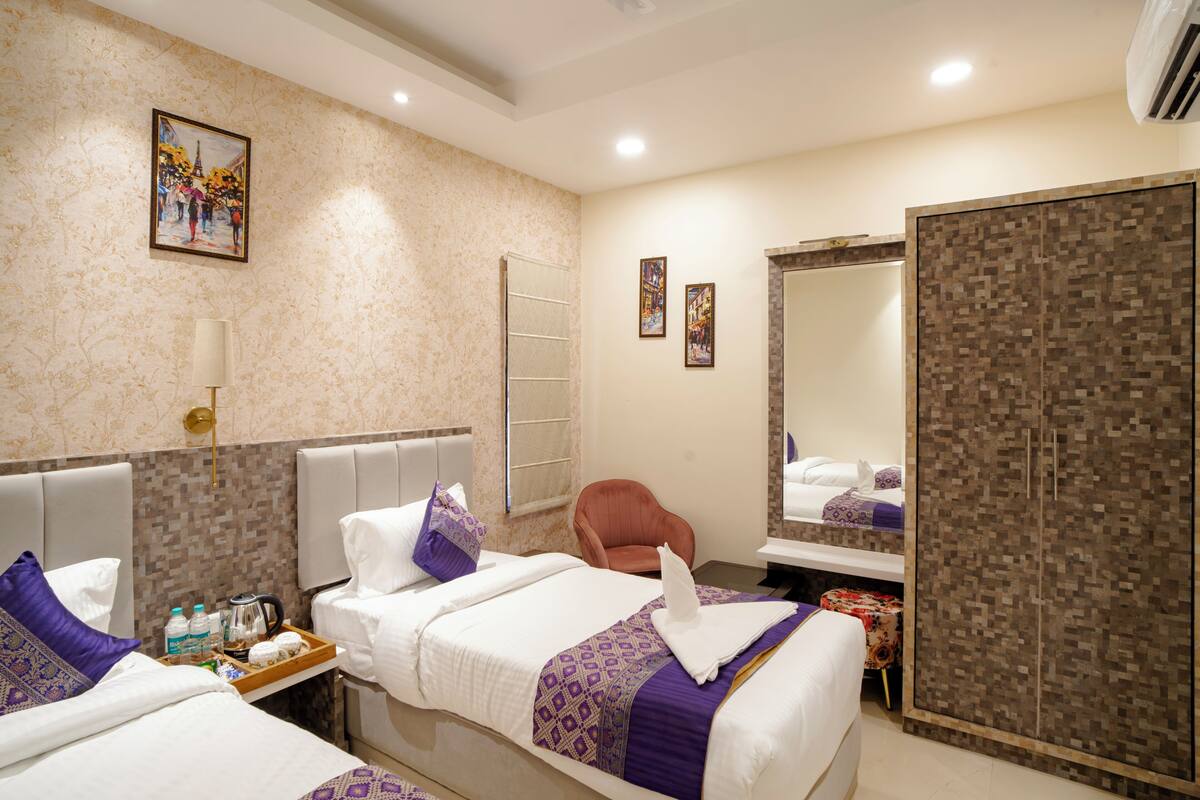 A hotel room with two beds, a chair, a small table with toiletries, a mirror, and a wardrobe.