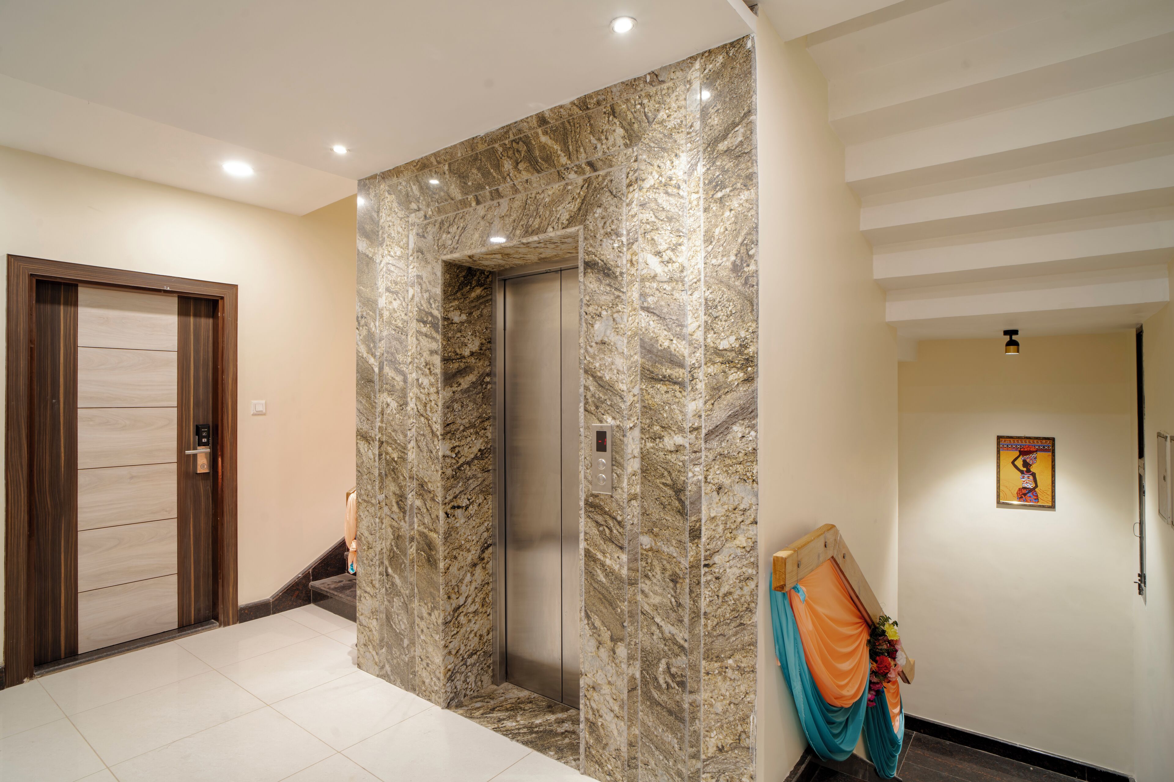 A modern elevator with marble walls, a wooden door, and a staircase leading to another floor.