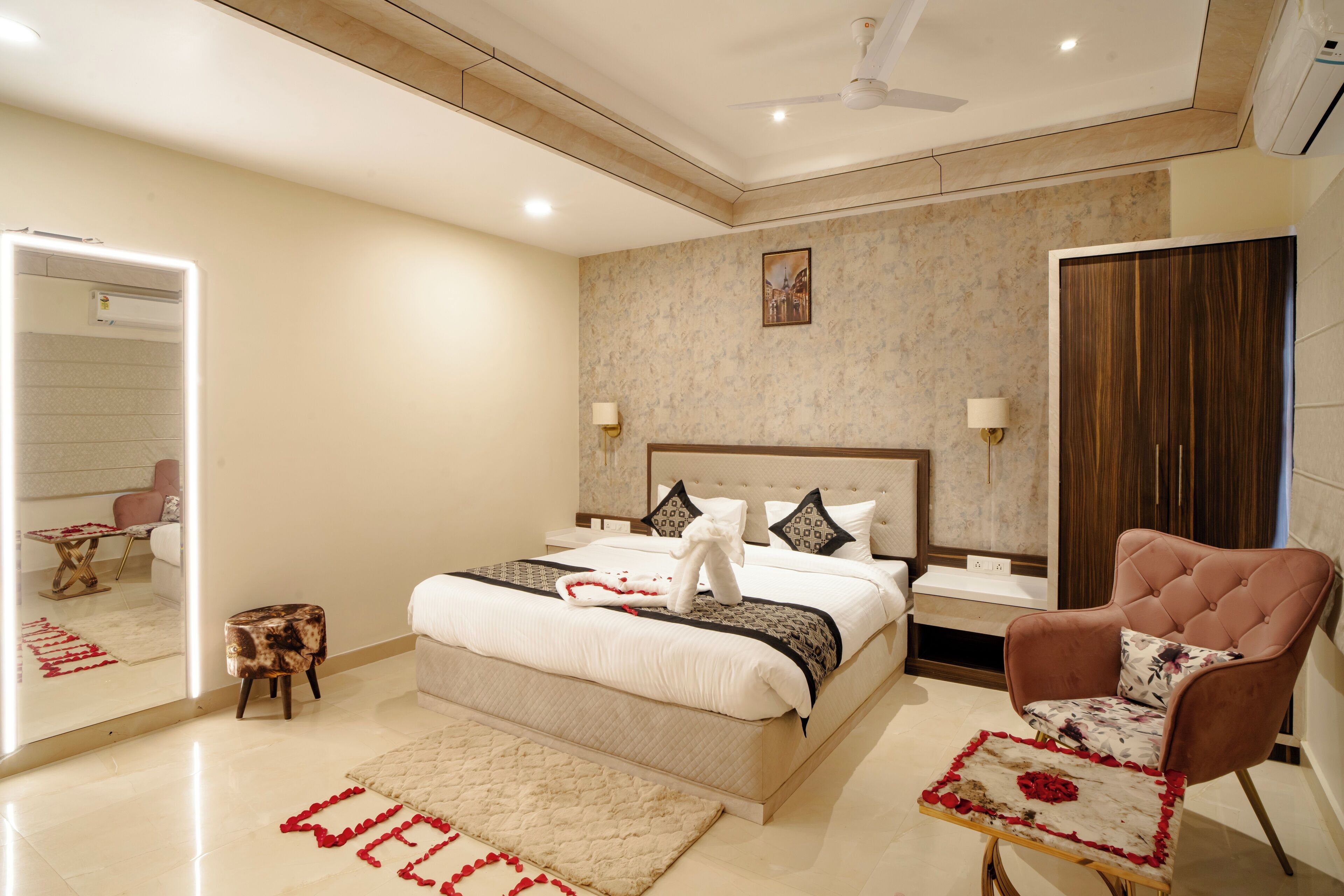 A modern bedroom with a large bed, a sitting area with a chair, a mirror, and a small table.
