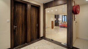 A room with two wooden doors, a glass partition, and a red fire hose on the wall. - Omkar International Hotel (VARANASI)