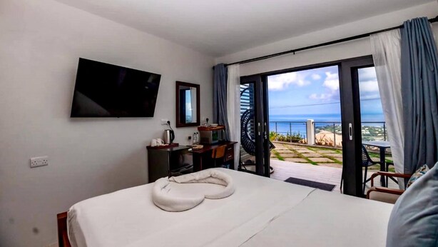 A hotel room with a bed, a TV, a desk, and a view of the ocean. - Hammock CoCo-Nut - by ZenBreak (Morne Fortune)