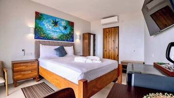 A modern hotel room with a wooden bed, a painting of a tropical scene, a desk, and a wardrobe.