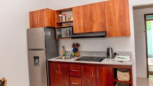 A compact kitchen with wooden cabinets, a stainless steel refrigerator, a microwave, and a sink.