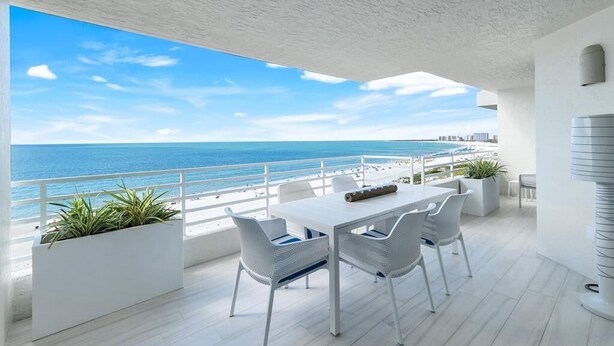 A balcony with a white table and chairs, overlooking a beach and ocean. - Beachfront 2BR/2BA Somerset condo with pool, WiFi, and heated pool. (Marco Island)