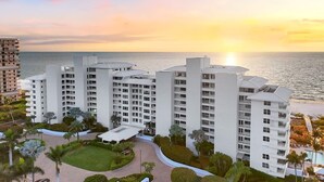 A high-rise hotel with multiple floors, a central courtyard, and a view of the ocean at sunset. - Beachfront 2BR/2BA Somerset condo with pool, WiFi, and heated pool. (Marco Island)