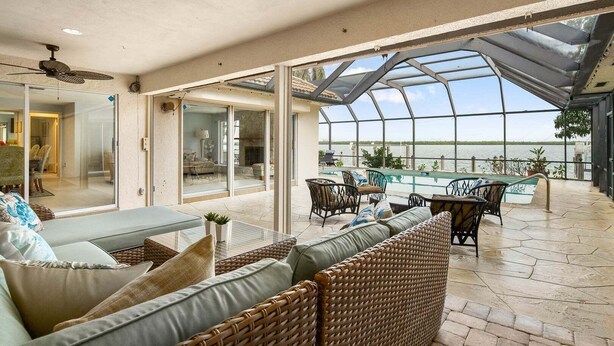 Ein großzügiger Patio-Bereich mit Glasdach, Gartenmöbeln und Blick auf das Wasser.