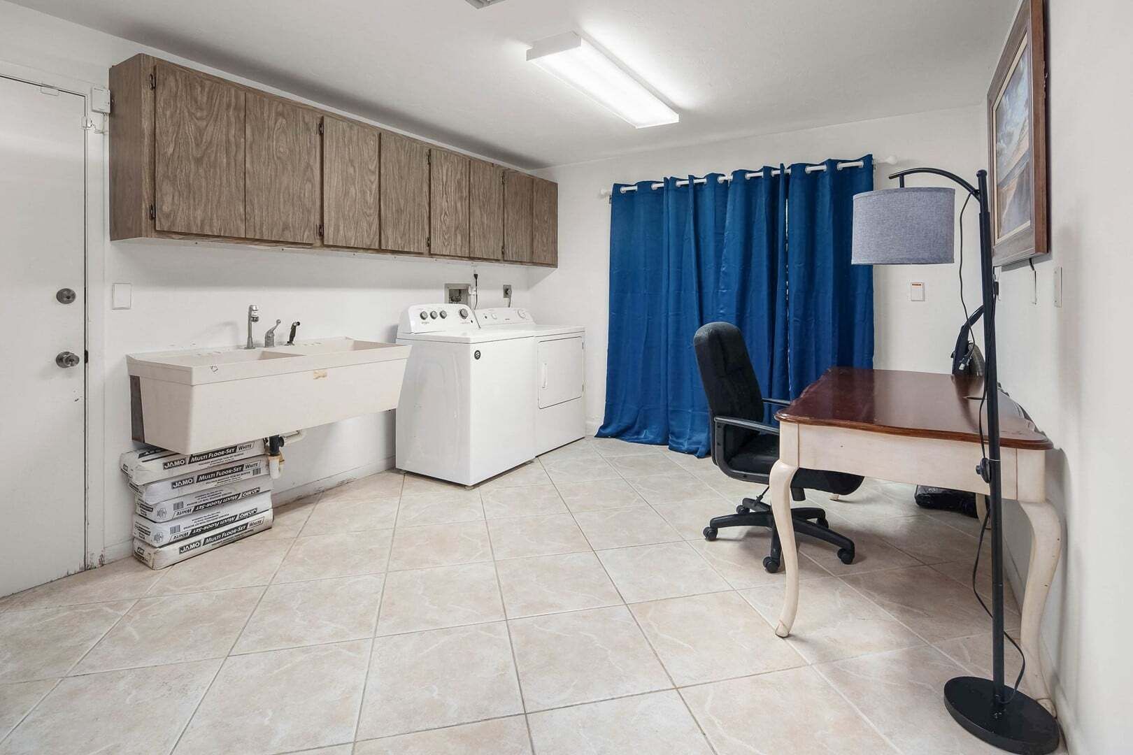 Een kleine kamer met een wasmachine, een wastafel, een bureau en een stoel.