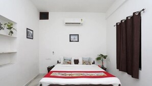 Een slaapkamer met een bed, een wandairconditioner, een donker gordijn en een kleine plant op de nachtkastje.
