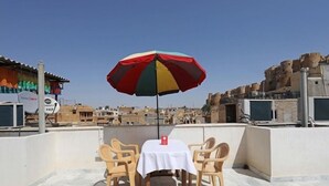 Een dakterras met een tafel en stoelen onder een kleurrijke parasol, met uitzicht op een stadsbeeld met traditionele architectuur.