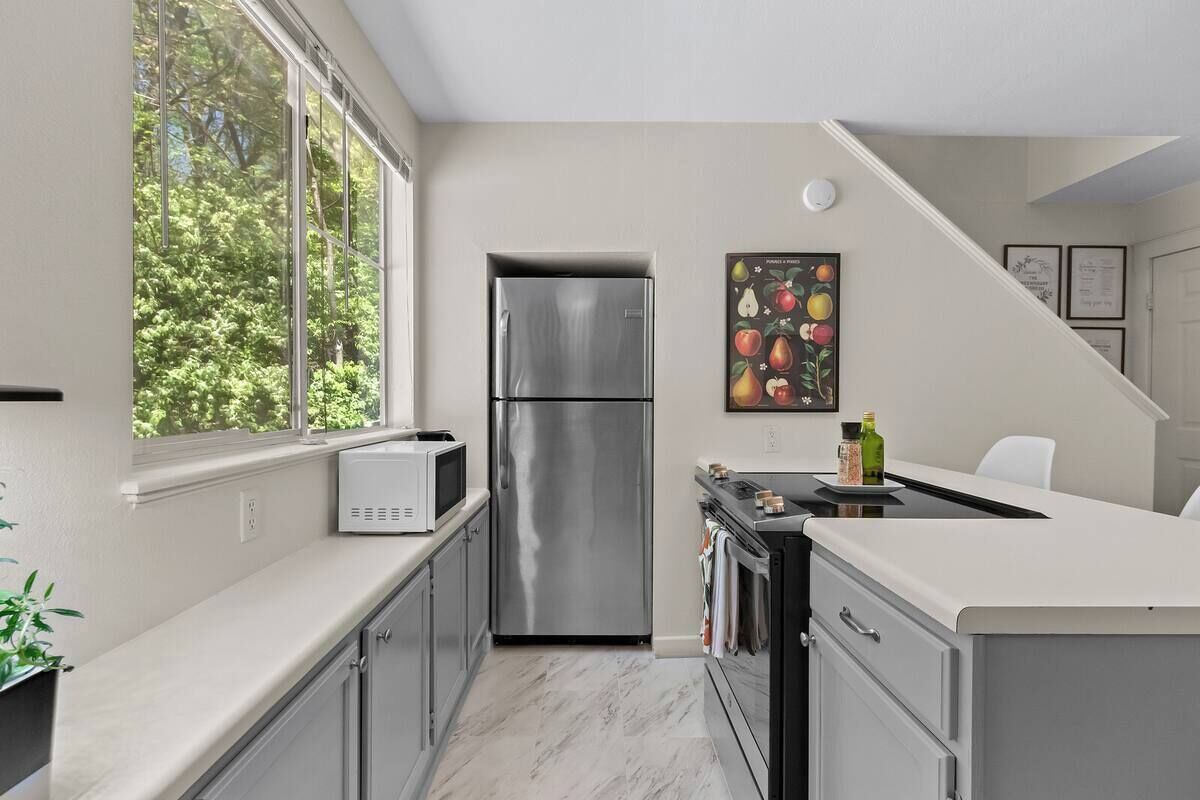 Una cocina moderna con un refrigerador de acero inoxidable, un microondas y una estufa. Hay una ventana que ofrece luz natural y vistas a los árboles.