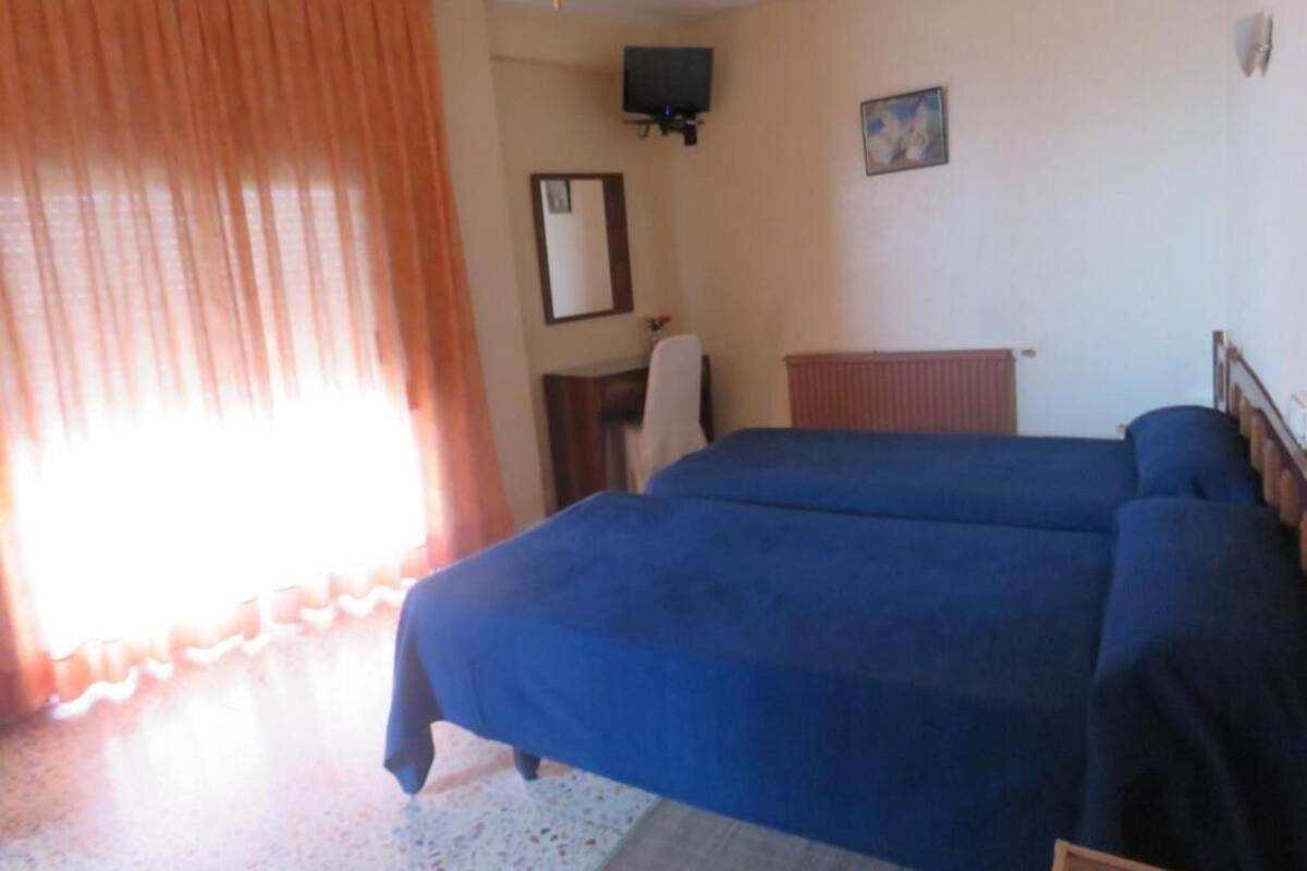 A room with two beds, a television on the wall, a mirror, and a window with curtains.