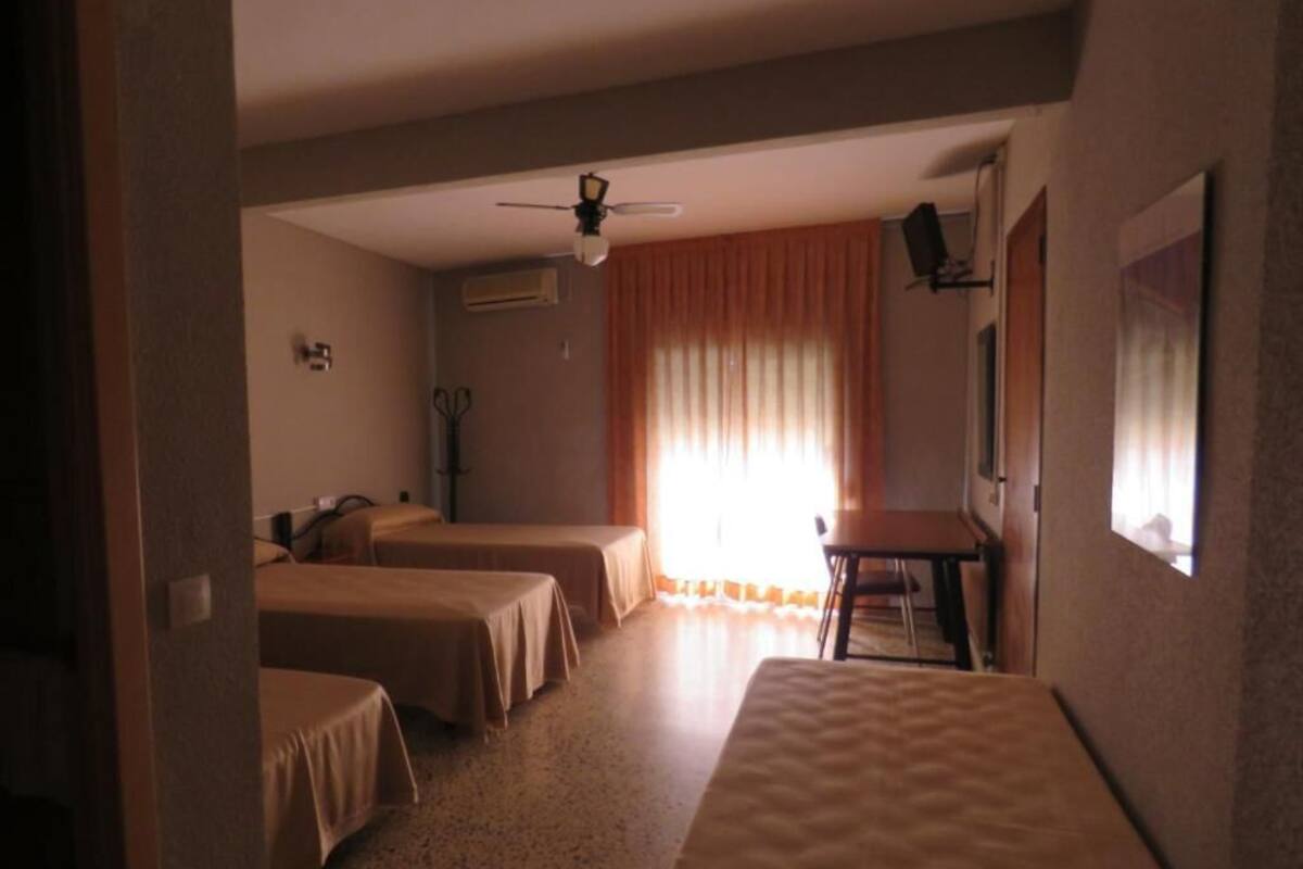 A hotel room with two single beds, a desk, a chair, a ceiling fan, and a window with curtains.