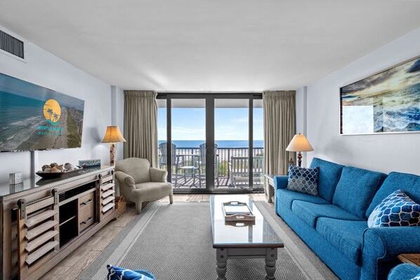 A modern living room with a large window, a blue sofa, a beige armchair, and a wooden sideboard.