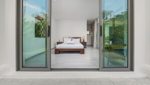 A modern bedroom with a large bed, sliding glass doors, and a view of greenery outside. - Villa Mauri Modern 3BR Private Pool (Rawai)