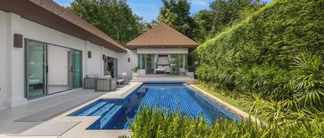 A modern house with a swimming pool, a patio with outdoor furniture, and a lush green garden.