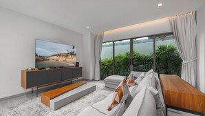A modern living room with a large flat-screen TV, a wooden coffee table, and a sofa with cushions. - Villa Mauri Modern 3BR Private Pool (Rawai)