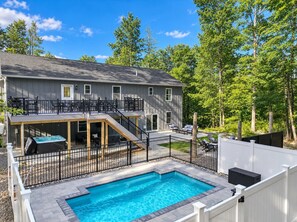 Une maison à deux étages avec une piscine dans le jardin, un patio couvert et une terrasse délimitée par une clôture.