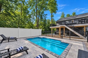 A backyard with a swimming pool, a covered patio, and a two-story house.