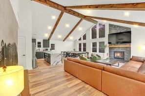 A spacious living area with a high ceiling, wooden beams, a fireplace, and a dining area.