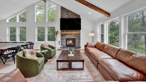 A spacious living room with a fireplace, large windows, and a high ceiling with exposed beams. - Private Pool Chalet | HotTub | Firepit | Game Room (Blakeslee)
