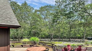 An outdoor patio with wooden tables and chairs, a fire pit, and a wooden deck.