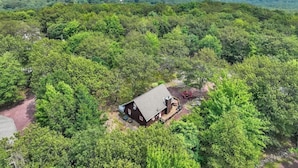 A single-story cabin surrounded by dense forest, with a clear view of the landscape in the background.
