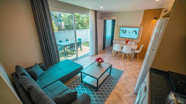 A modern living room with a sofa, coffee table, and a dining area with chairs and a table. - Moon Suites (Antalya)