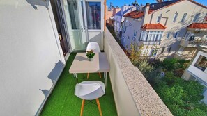A small balcony with a table and two chairs, a potted plant, and a view of neighboring buildings. - Moon Suites (Antalya)