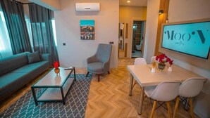A modern living room with a sofa, armchair, coffee table, and dining area with chairs and a TV displaying 'MOON suites'. - Moon Suites (Antalya)