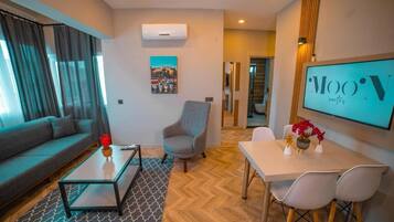 Una sala de estar moderna con sofá, sillón, mesa de centro y zona de comedor con sillas, y un televisor mostrando 'MOON suites'.