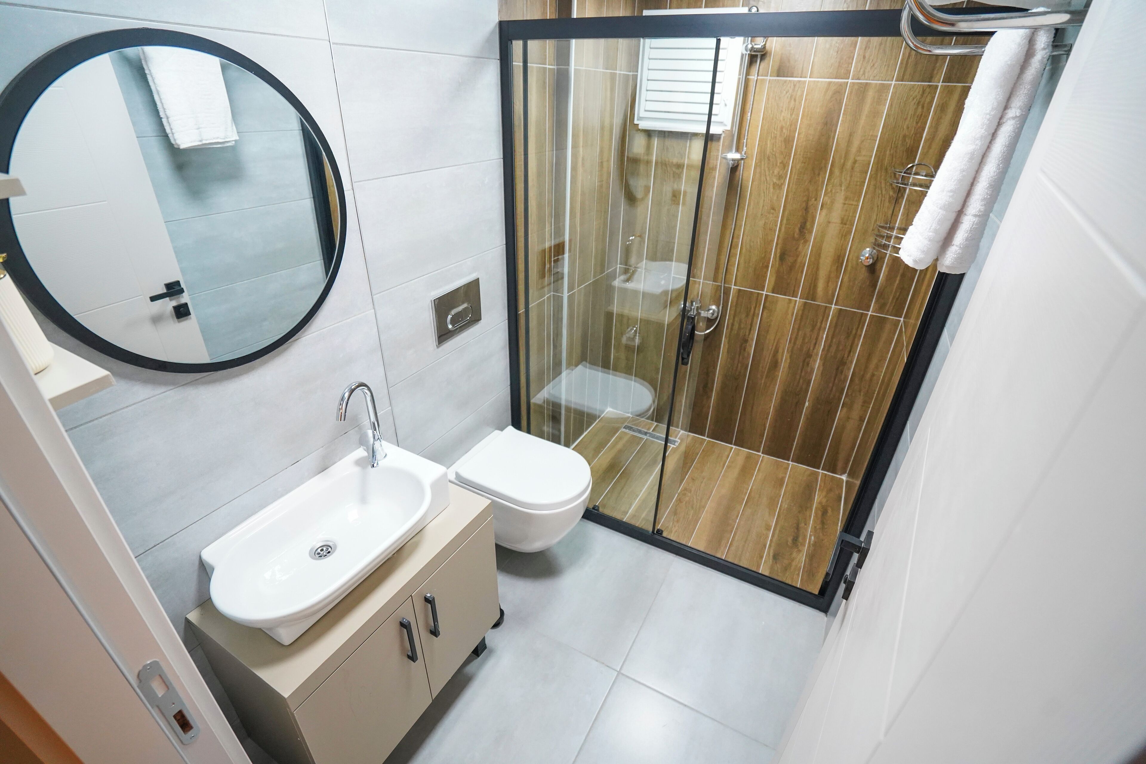 A modern bathroom with a round mirror, a sink, a toilet, and a glass-enclosed shower.