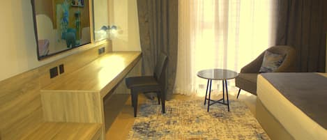 A hotel room with a bed, a desk, a chair, a small table, and a large mirror.
