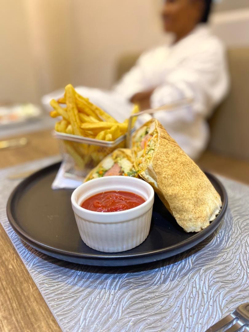 A plate with a wrap sandwich, a small bowl of sauce, and a container of fries.