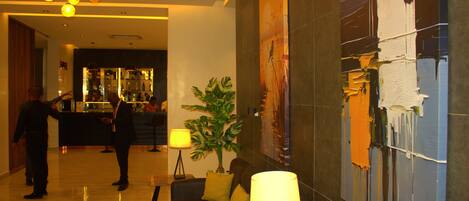 A lobby with a bar area, a seating area with a sofa and a lamp, and a large abstract painting on the wall.
