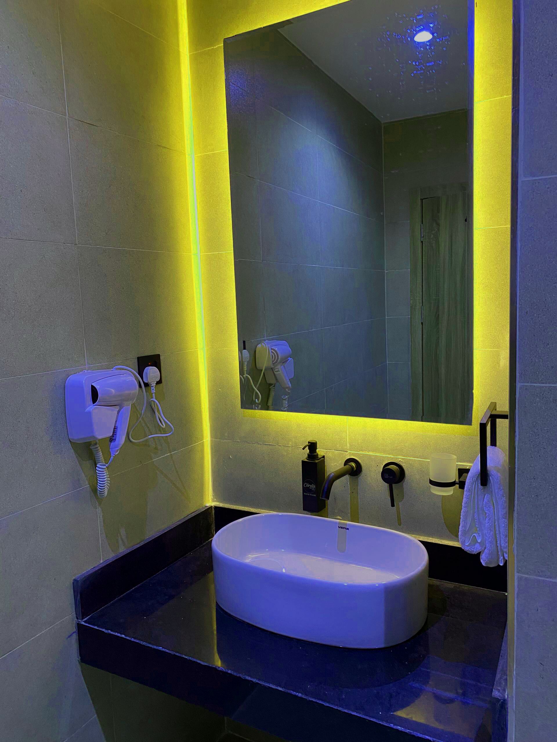 A modern bathroom with a large mirror, a white sink, and a hairdryer mounted on the wall.