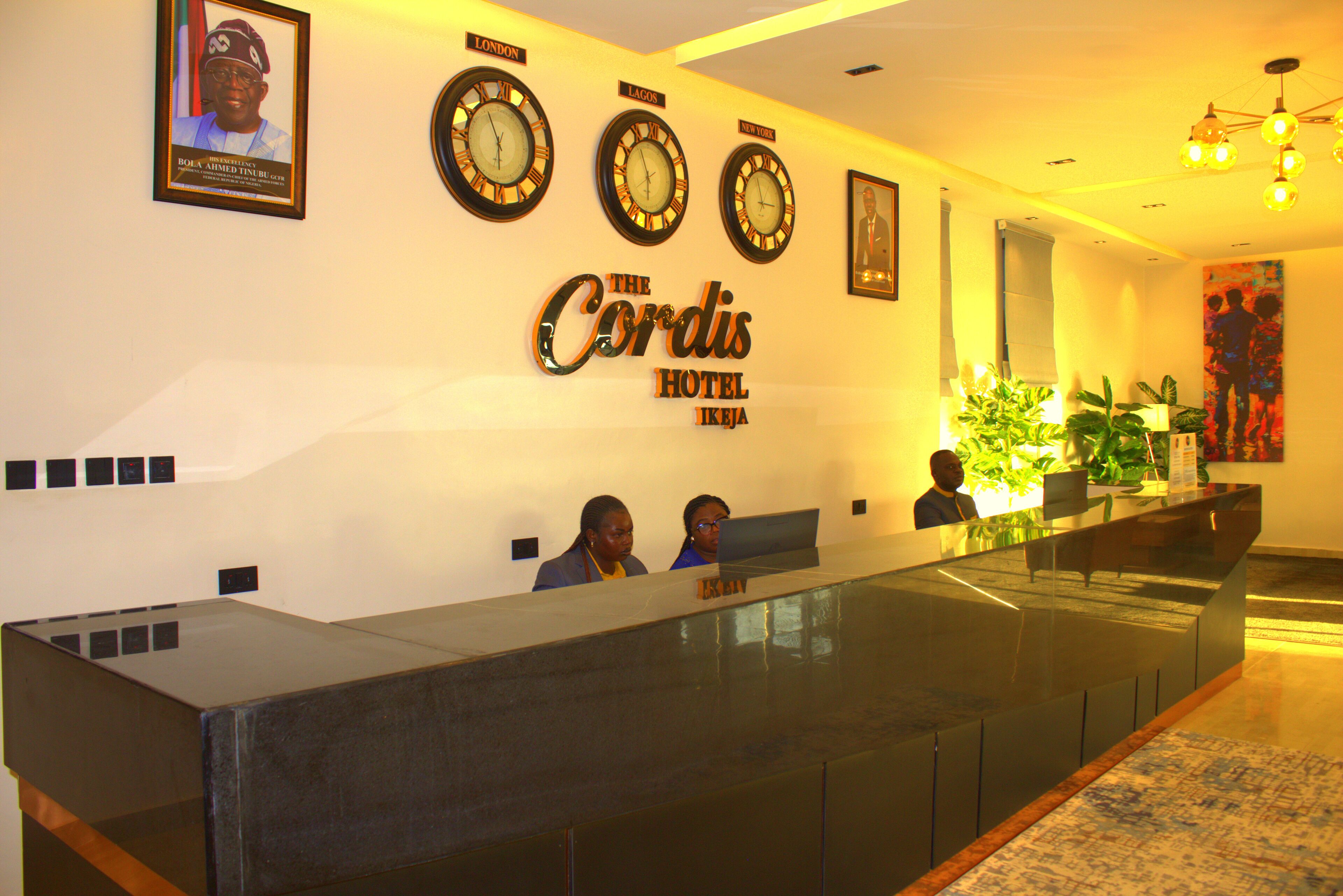 A hotel reception desk with clocks displaying different time zones, a receptionist, and a receptionist's computer.