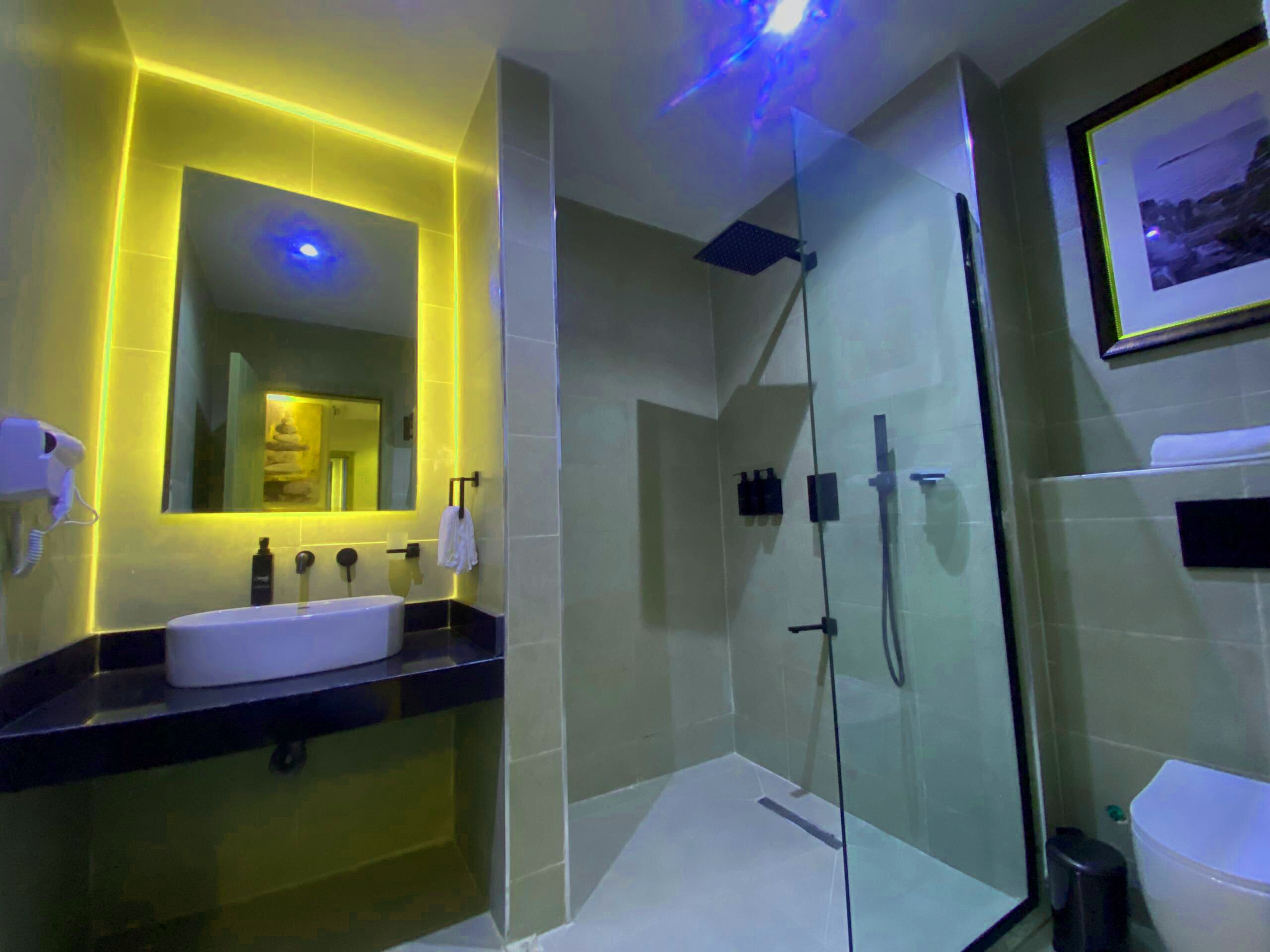 A modern bathroom with a glass-enclosed shower, a white sink, and a mirror with yellow lighting.