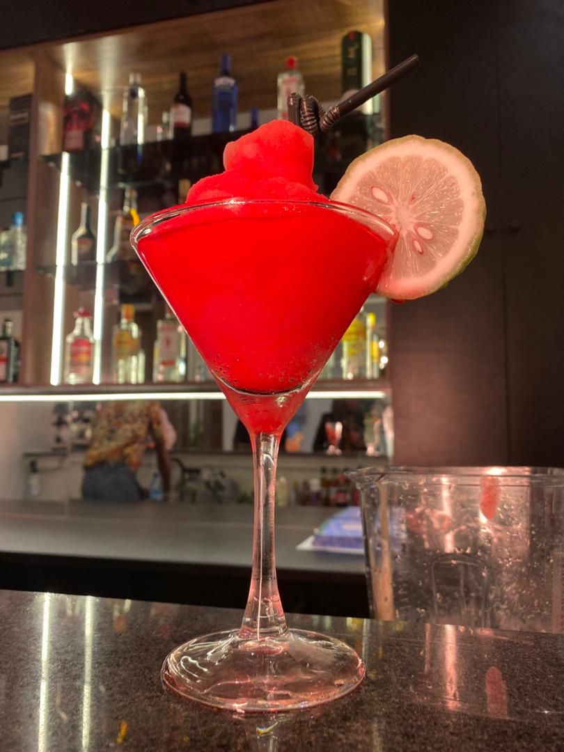 A martini glass with a red cocktail, garnished with a slice of lime, on a bar counter.