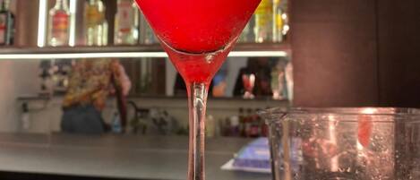 A martini glass with a red cocktail, garnished with a slice of lime, on a bar counter.