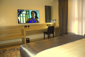 Une chambre d’hôtel équipée d’un lit, d’un bureau, d’une chaise, d’une télévision et d’une fenêtre avec des rideaux.
