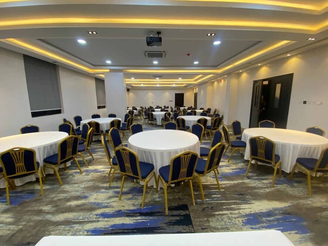 A conference room with round tables and blue chairs, equipped with ceiling projectors and recessed lighting.